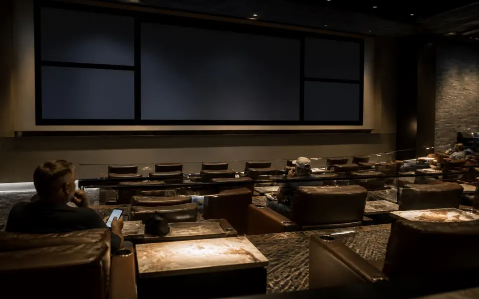 Illustration: a sportsbook lounge with a wall of blank screens and tiered leather seating