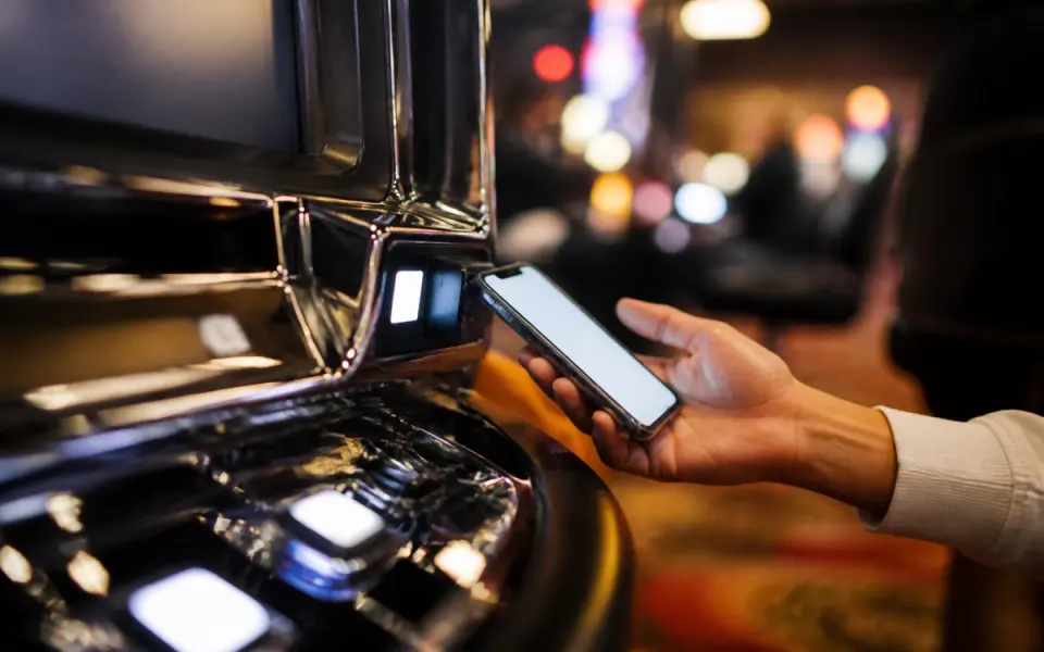 Illustration: a hand holding a phone up to the card reader on a slot machine