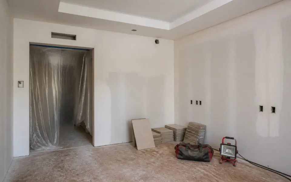 Illustration: a hotel guest room mid-renovation, stripped to new drywall behind plastic sheeting